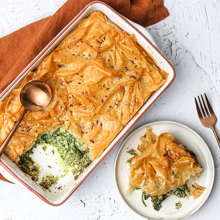 Spinach and Ricotta Filo Bake in a dish with a serving on a plate, on a white background.