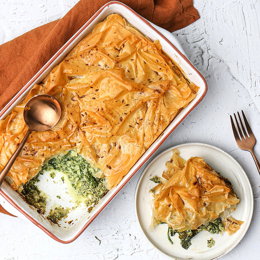 Spinach and Ricotta Filo Bake in a dish with a serving on a plate, on a white background.